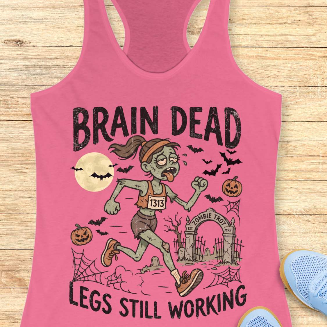 pink Halloween tank top with an image of a running zombie and text 'Brain dead legs still working', on a wooden surface