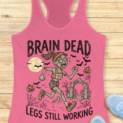 pink Halloween tank top with an image of a running zombie and text 'Brain dead legs still working', on a wooden surface