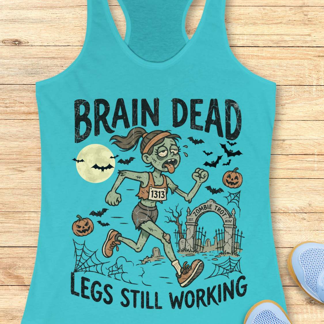 blue Halloween tank top with an image of a running zombie and text 'Brain dead legs still working', on a wooden surface