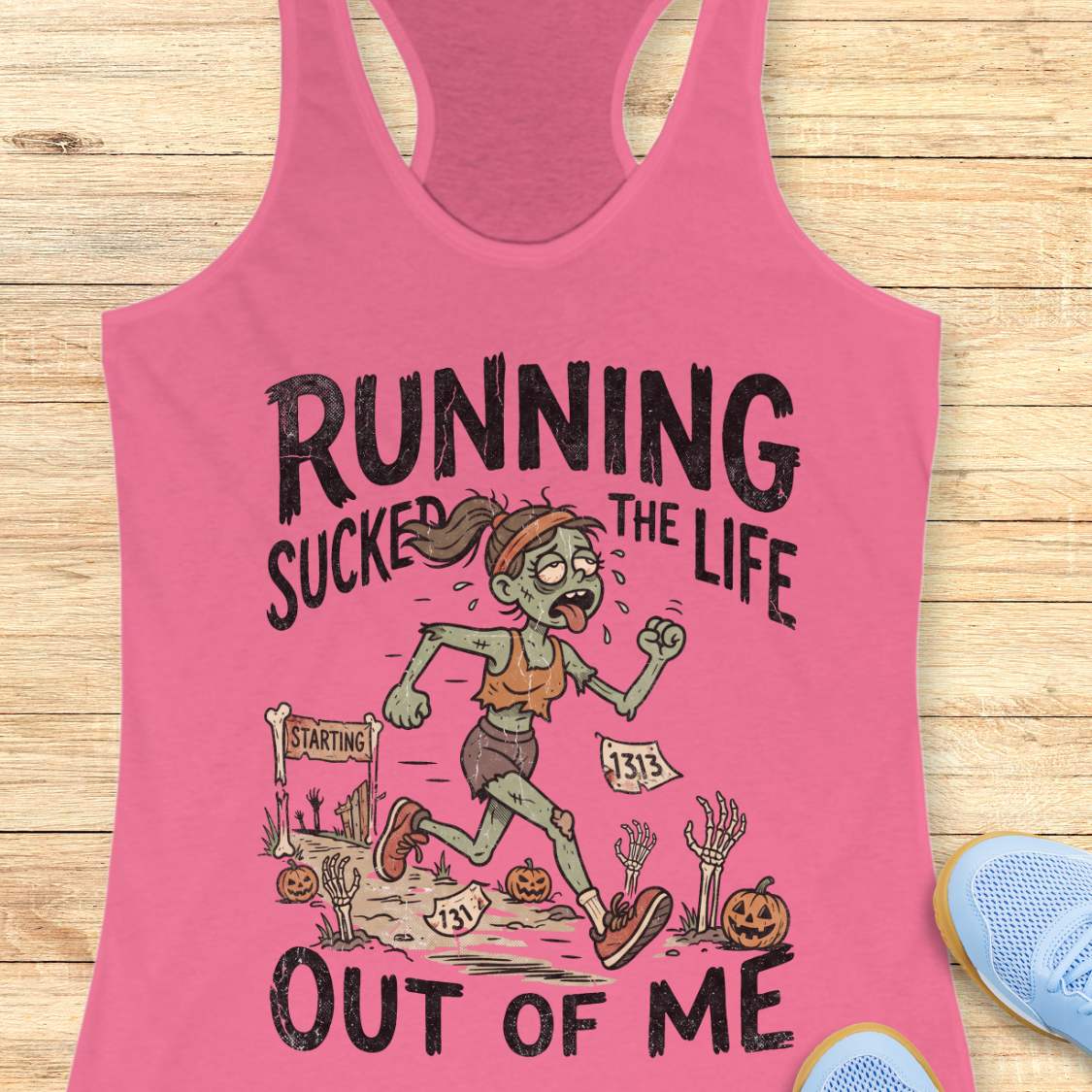 pink Halloween tank top with an image of a running zombie and text 'Running sucked the life out of me', on a wooden surface