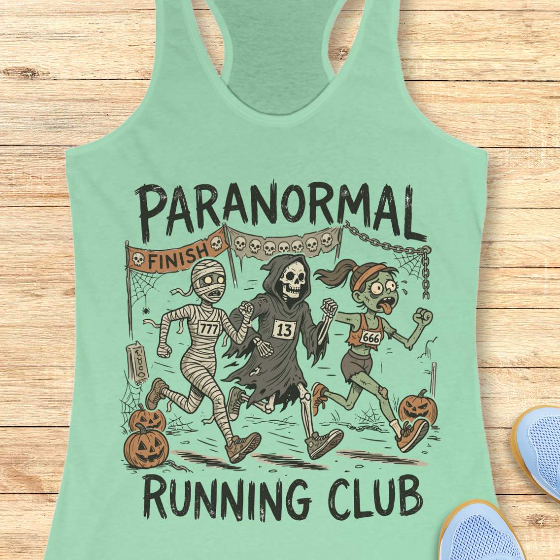 mint Halloween tank top with an image of a running zombie, mummy and reaper,  and text 'Paranormal running club', on a wooden surface