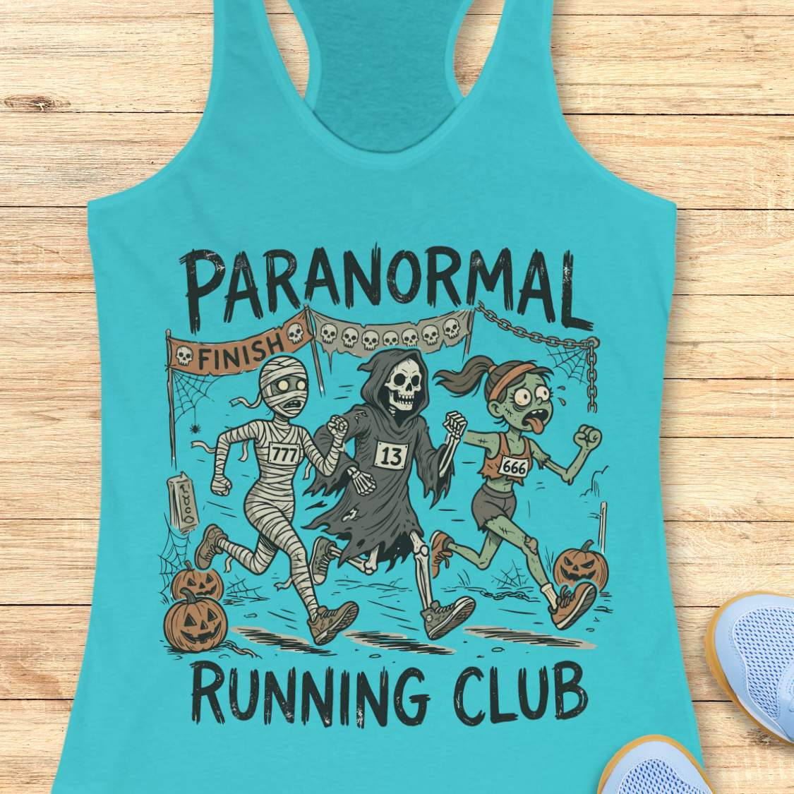 blue Halloween tank top with an image of a running zombie, mummy and reaper,  and text 'Paranormal running club', on a wooden surface