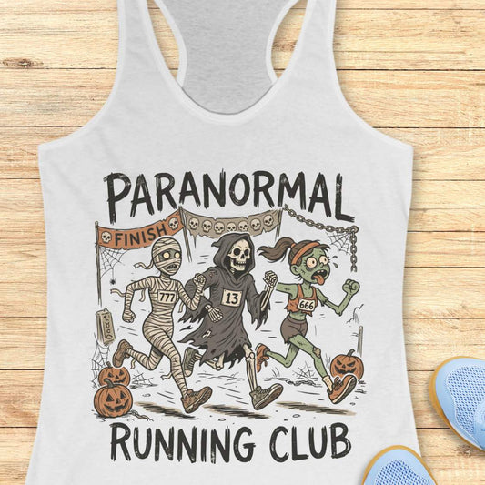 white Halloween tank top with an image of a running zombie, mummy and reaper,  and text 'Paranormal running club', on a wooden surface