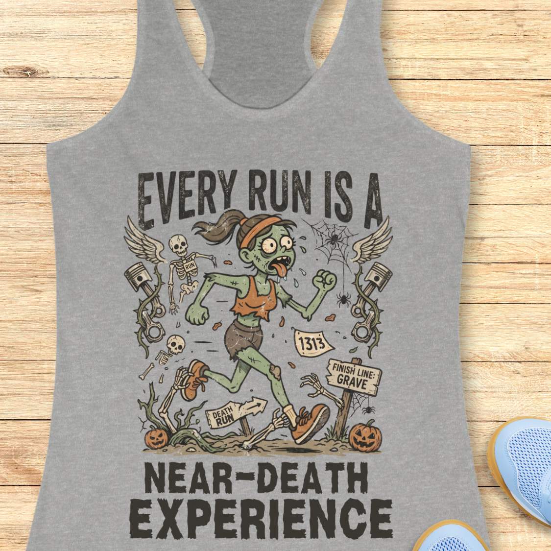 grey Halloween tank top with an image of a running zombie and text 'Every run is a near-death experience', on a wooden surface
