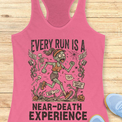 pink Halloween tank top with an image of a running zombie and text 'Every run is a near-death experience', on a wooden surface