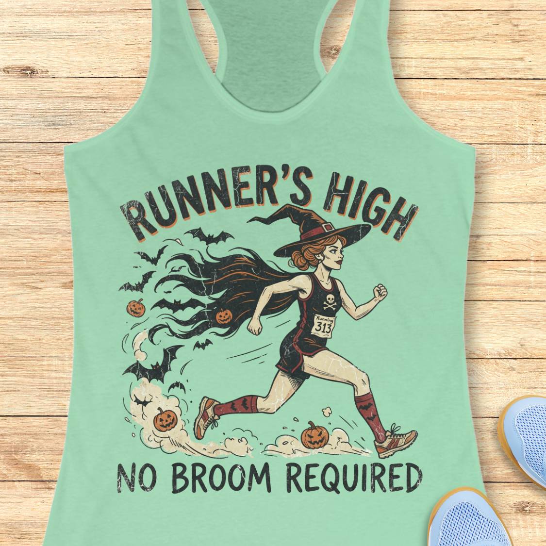 A mint green racerback tank top featuring a graphic of a witch running with pumpkins and bats, with the text 'RUNNER'S HIGH' and 'NO BROOM REQUIRED'. The tank top is displayed flat on a light wood background with partial blue shoes visible in the corners.