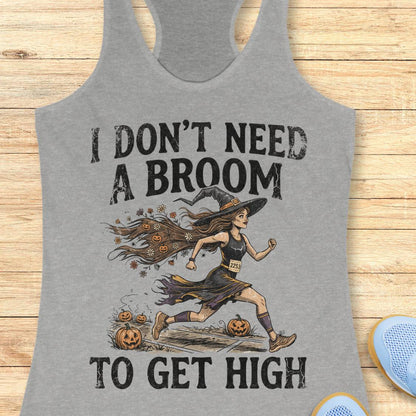 A heather gray racerback tank top laid flat on a light wood surface, featuring a Halloween graphic of a witch running with pumpkins and the text 'I DON'T NEED A BROOM TO GET HIGH'.