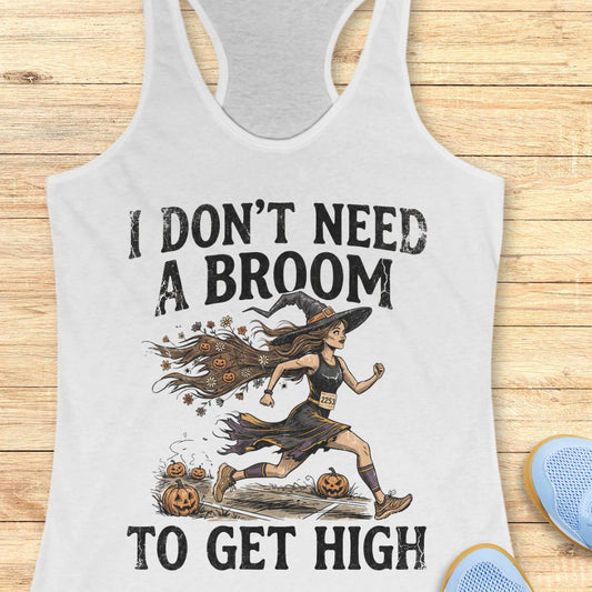 A white racerback tank top with a Halloween graphic of a witch running with pumpkins, with the text 'I DON'T NEED A BROOM TO GET HIGH', displayed flat on a light wood background.