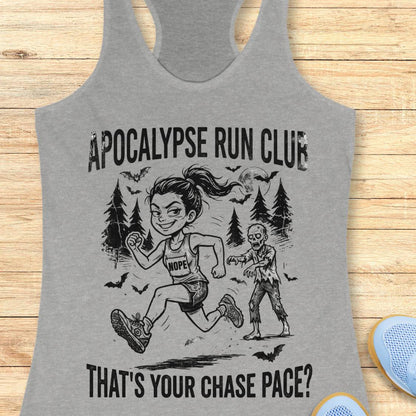 A heather gray racerback tank top laid flat on a light wood surface, featuring a black graphic print of a woman running with a zombie and the text 'APOCALYPSE RUN CLUB' and 'THAT'S YOUR CHASE PACE?'.