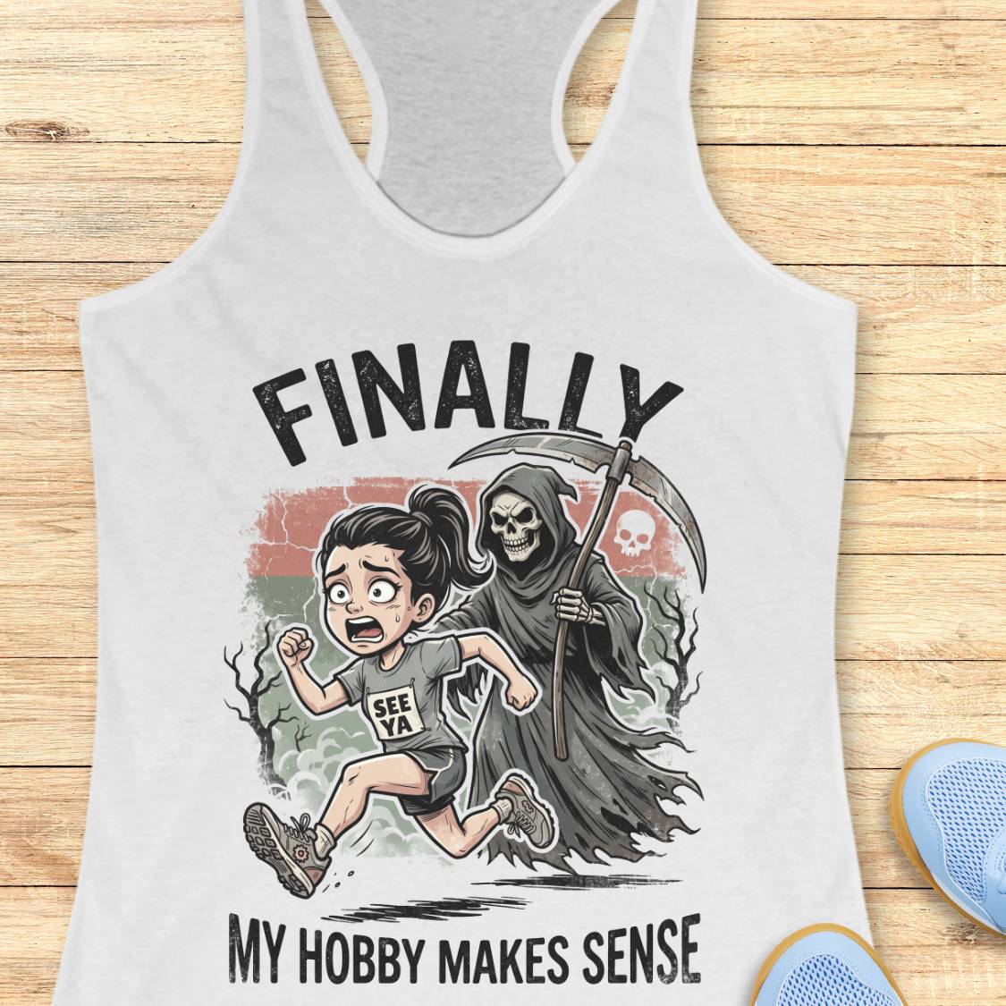 A white racerback tank top laid flat on a light wood background, featuring a cartoon graphic of a girl running while being chased by a grim reaper, with the text 'FINALLY MY HOBBY MAKES SENSE'.