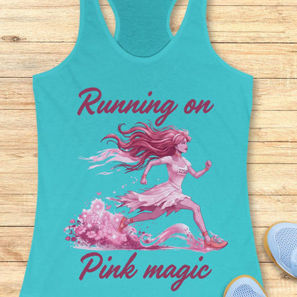 A turquoise racerback tank top laid flat on a light wood surface, featuring a pink graphic of a running woman with the text 'Running on Pink magic.' A light blue shoe is partially visible at the bottom right as a styling prop.