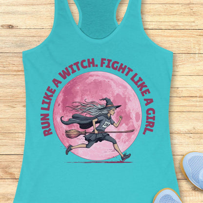 A turquoise racerback tank top laid flat on a light wood surface, featuring a large graphic of a witch running on a broomstick in front of a pink full moon, with the text 'RUN LIKE A WITCH. FIGHT LIKE A GIRL' in pink around the design.