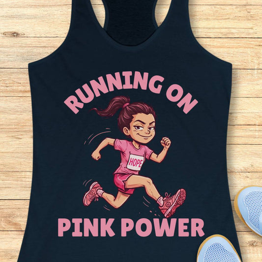 A navy racerback tank top laid flat on a light wood surface, featuring a cartoon illustration of a running woman in pink with the text 'RUNNING ON PINK POWER' in pink. Part of a light blue shoe is visible at the bottom right.