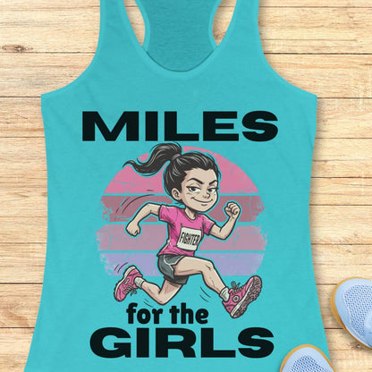 A turquoise racerback tank top laid flat on a light wood surface, featuring a cartoon girl running with the text 'MILES for the GIRLS' in black. A partial blue shoe is visible at the bottom right.