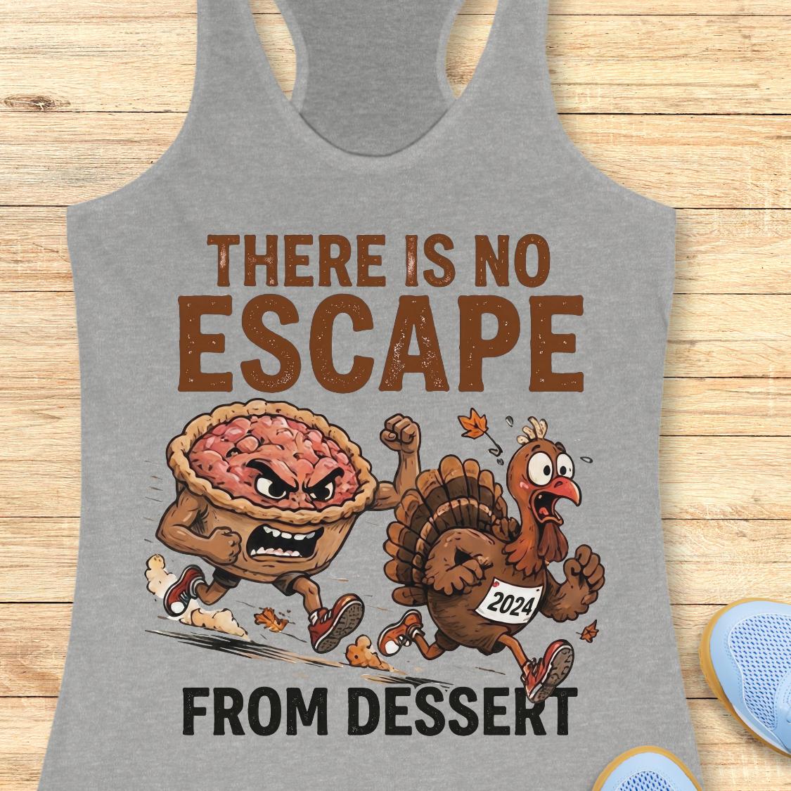 A heather gray racerback tank top laid flat on a light wood surface, featuring a Thanksgiving-themed graphic with the text 'THERE IS NO ESCAPE FROM DESSERT' and an illustration of an angry pie and a cartoon turkey running away. Partial blue shoes are visible at the bottom right edge.