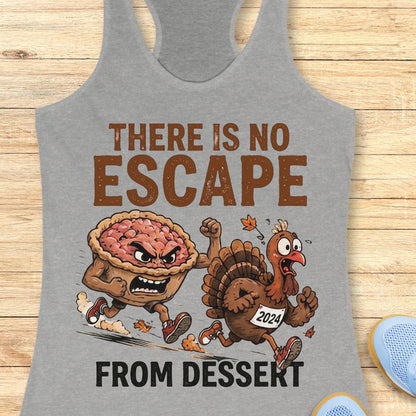 A heather gray racerback tank top laid flat on a light wood surface, featuring a Thanksgiving-themed graphic with the text 'THERE IS NO ESCAPE FROM DESSERT' and an illustration of an angry pie and a cartoon turkey running away. Partial blue shoes are visible at the bottom right edge.