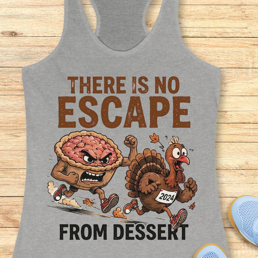A heather gray racerback tank top laid flat on a light wood surface, featuring a Thanksgiving-themed graphic with the text 'THERE IS NO ESCAPE FROM DESSERT' and an illustration of an angry pie and a cartoon turkey running away. Partial blue shoes are visible at the bottom right edge.