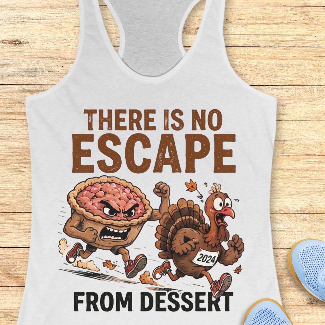 A white racerback tank top laid flat on a light wood surface, featuring a cartoon graphic of an angry pie and a running turkey with the text 'THERE IS NO ESCAPE FROM DESSERT.' A blue shoe is partially visible at the lower right edge.