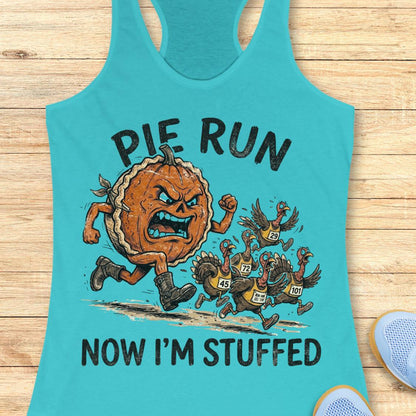 A turquoise racerback tank top laid flat on a light wood surface, featuring a cartoon graphic of an angry pie running and several turkeys, with the text 'PIE RUN NOW I'M STUFFED.' A partial blue shoe is visible at the lower right edge.