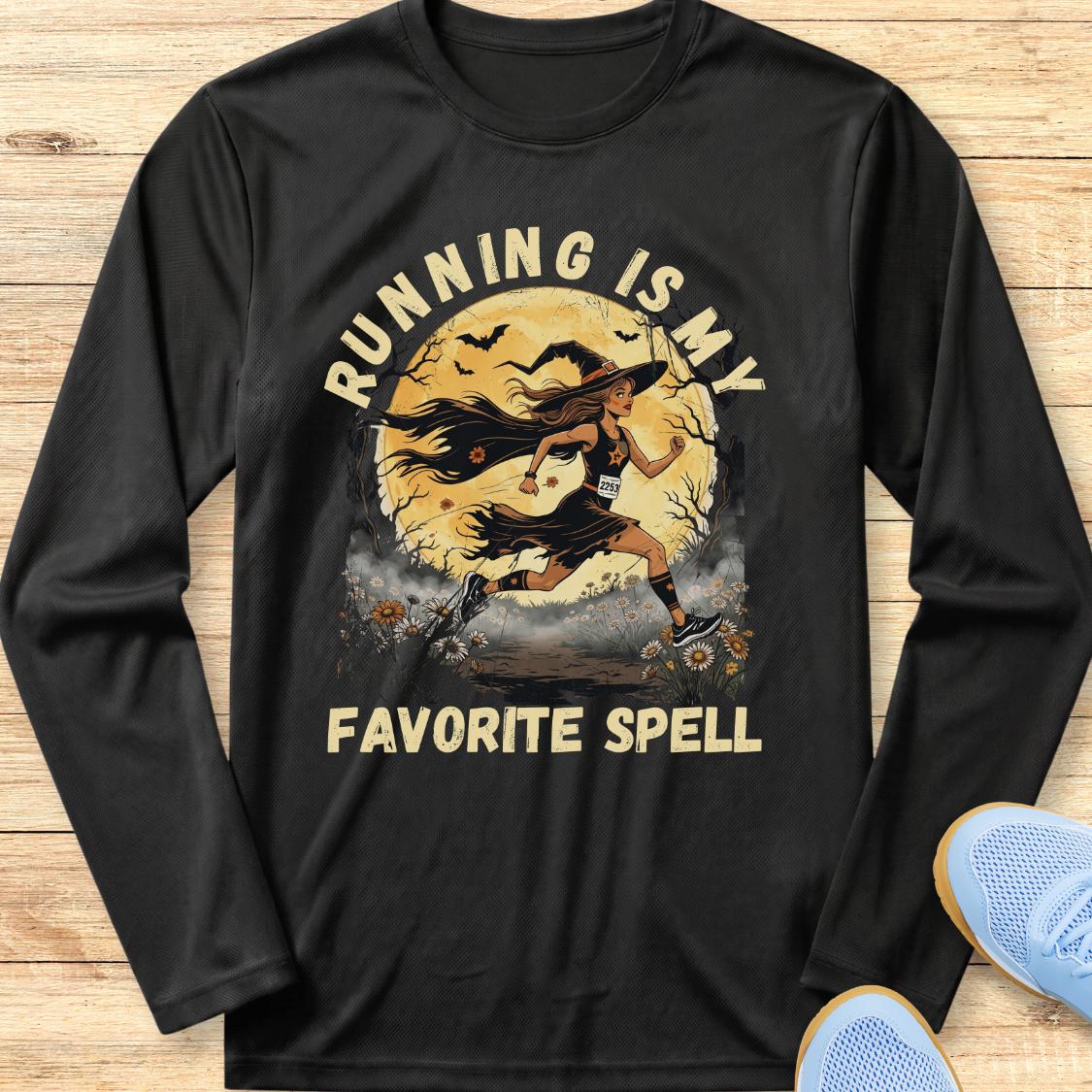 A black long-sleeve t-shirt with a graphic print of a witch running with a staff in front of a full moon, with the text 'RUNNING IS MY FAVORITE SPELL' in beige. The shirt is laid flat on a light wood background with blue sneakers partially visible in the corner.