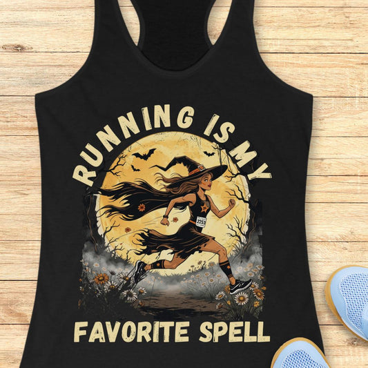 A black racerback tank top laid flat on a light wood surface, featuring a large graphic print of a witch running in front of a full moon with the text 'RUNNING IS MY FAVORITE SPELL.' Part of a blue shoe is visible at the bottom right as a styling prop.