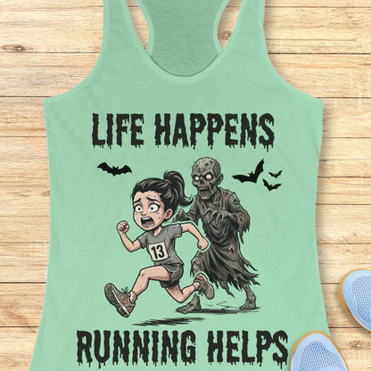 A mint green racerback tank top laid flat on a light wood background, featuring a cartoon graphic of a girl running beside a zombie with the text 'LIFE HAPPENS RUNNING HELPS'.