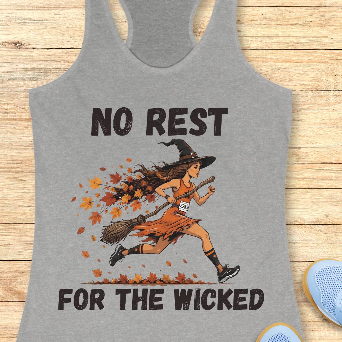 A heather gray racerback tank top featuring a graphic of a woman running a 5K while dressed as a witch, with the text 'NO REST FOR THE WICKED' in black. The tank top is displayed flat on a light wood background with a pair of blue sneakers partially visible at the bottom right.