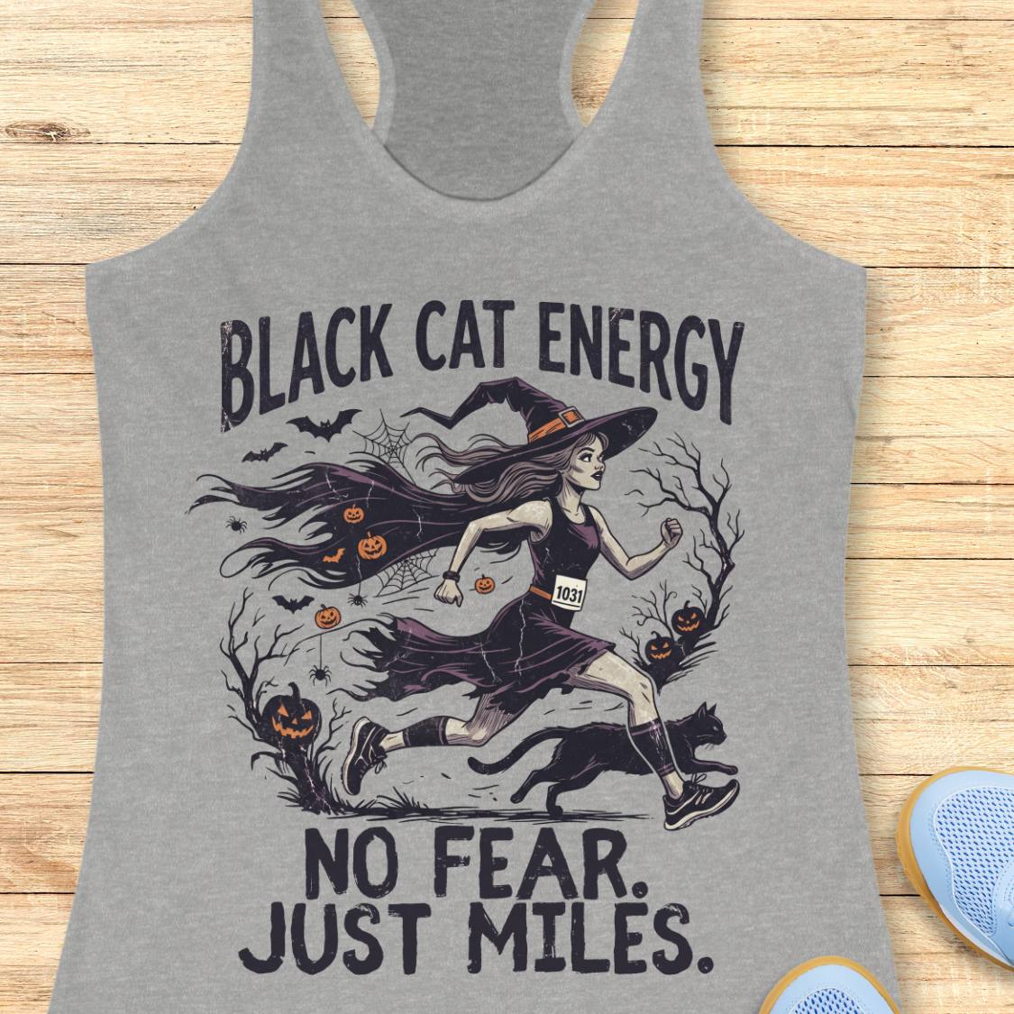 A heather gray racerback tank top featuring a Halloween-themed graphic of a witch running with a black cat, pumpkins, bats, and the text 'BLACK CAT ENERGY NO FEAR. JUST MILES.