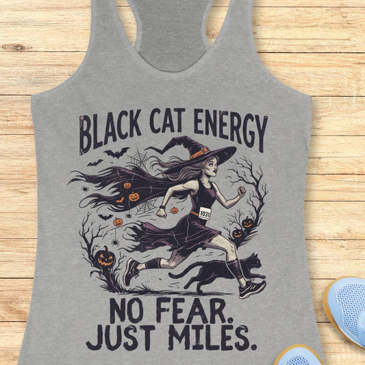 A heather gray racerback tank top featuring a Halloween-themed graphic of a witch running with a black cat, pumpkins, bats, and the text 'BLACK CAT ENERGY NO FEAR. JUST MILES.