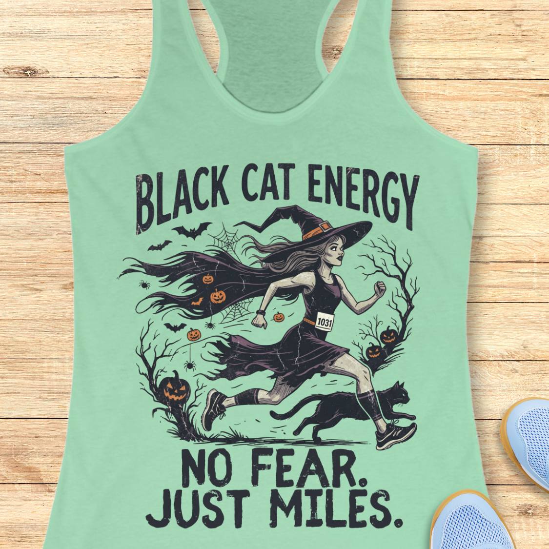 A mint green racerback tank top featuring a Halloween graphic of a witch running with a black cat, with the text 'BLACK CAT ENERGY NO FEAR. JUST MILES.