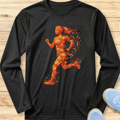 A black long-sleeve crewneck t-shirt featuring a graphic of a running woman composed of orange and yellow fire-like shapes, laid flat on a light wood background with light blue sneakers partially visible in the corner.