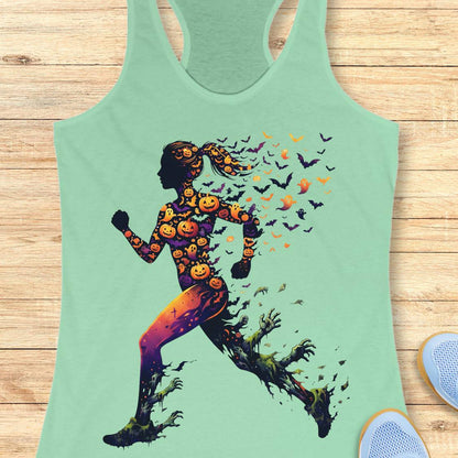 A mint green racerback tank top featuring a graphic of a running silhouette filled with jack-o'-lanterns and small bats, laid flat on a light wood background.