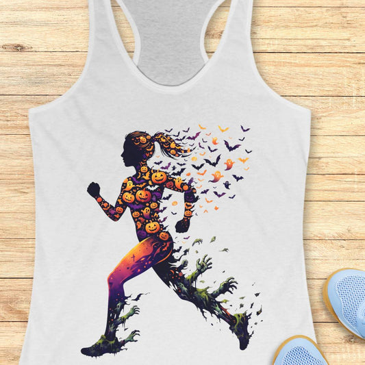 A white racerback tank top laid flat on a light wood surface, featuring a large graphic of a running silhouette filled with orange pumpkins and bats, with green vines trailing from the feet. Part of a blue shoe is visible at the bottom right.