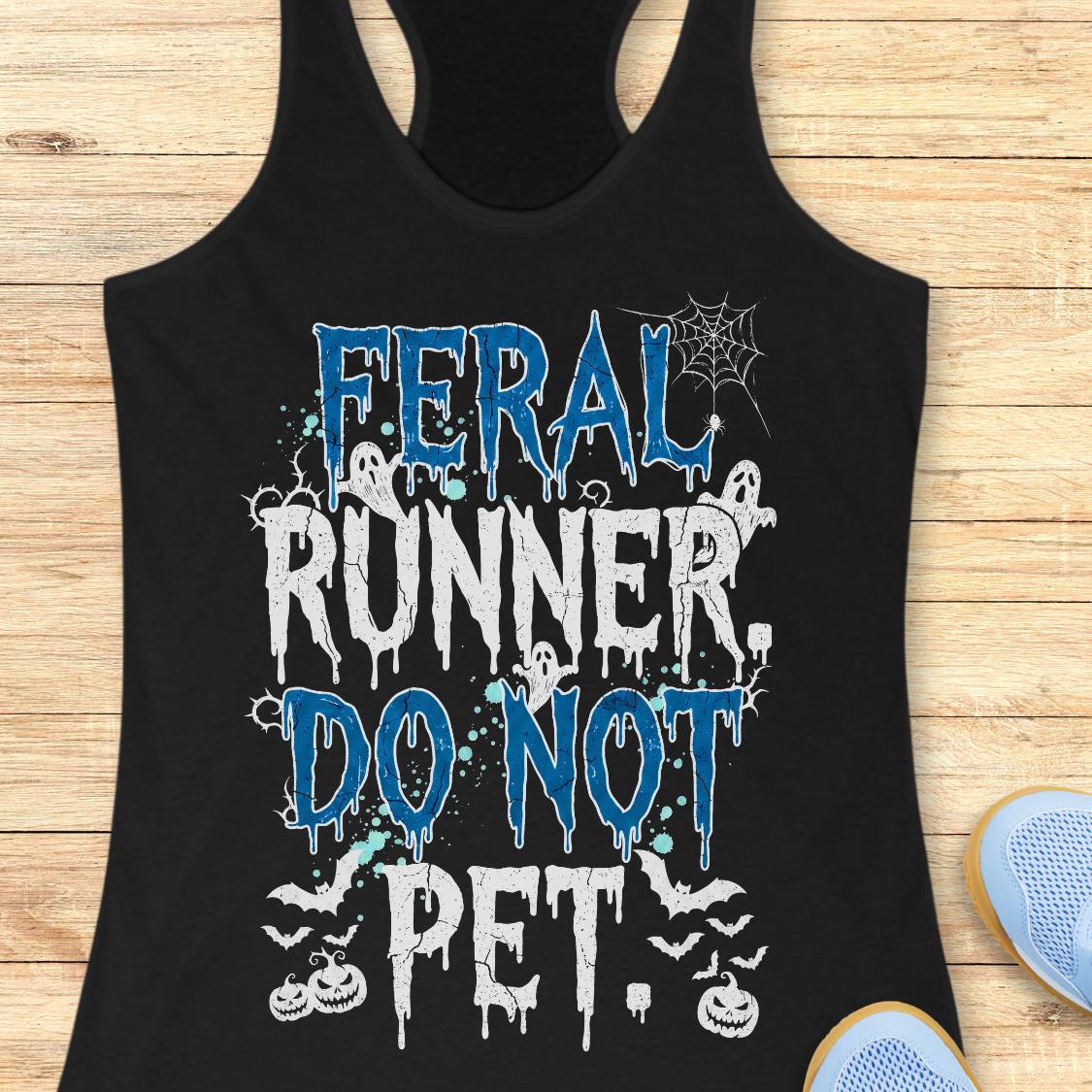 A black racerback tank top laid flat on a light wood surface, featuring a Halloween-themed graphic that reads 'FERAL RUNNER, DO NOT PET.' in blue and white dripping lettering with ghosts, bats, spiderwebs, and pumpkins.