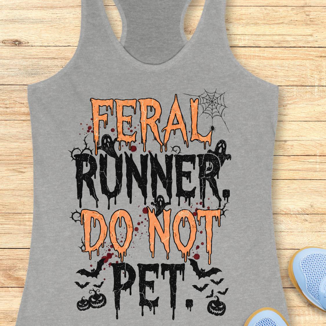 A heather gray racerback tank top with a Halloween-themed graphic reading 'FERAL RUNNER, DO NOT PET' in orange and black dripping lettering, styled flat on a light wood background with partial blue shoes visible at the edges.
