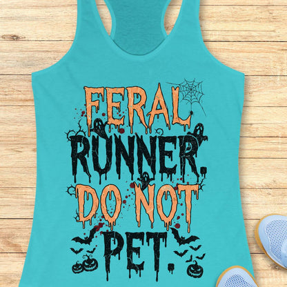 A turquoise racerback tank top laid flat on a light wood surface, featuring a Halloween-themed graphic that reads 'FERAL RUNNER, DO NOT PET' in orange and black dripping lettering with spiderwebs, ghosts, bats, and pumpkins.