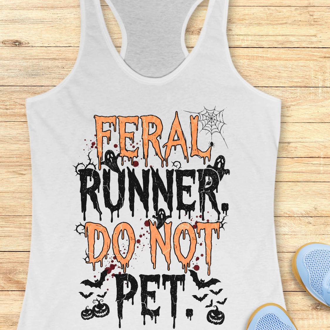 A white racerback tank top laid flat on a light wood surface, featuring a Halloween-themed graphic that reads 'FERAL RUNNER, DO NOT PET.' in orange and black dripping lettering with spiderwebs, ghosts, bats, and pumpkins.