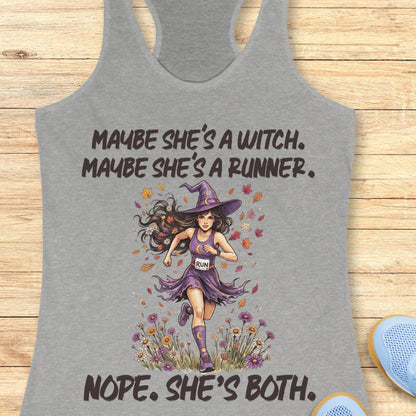 A heather gray racerback tank top laid flat on a light wood background, featuring a graphic of a witch running with the text 'MAYBE SHE'S A WITCH. MAYBE SHE'S A RUNNER.