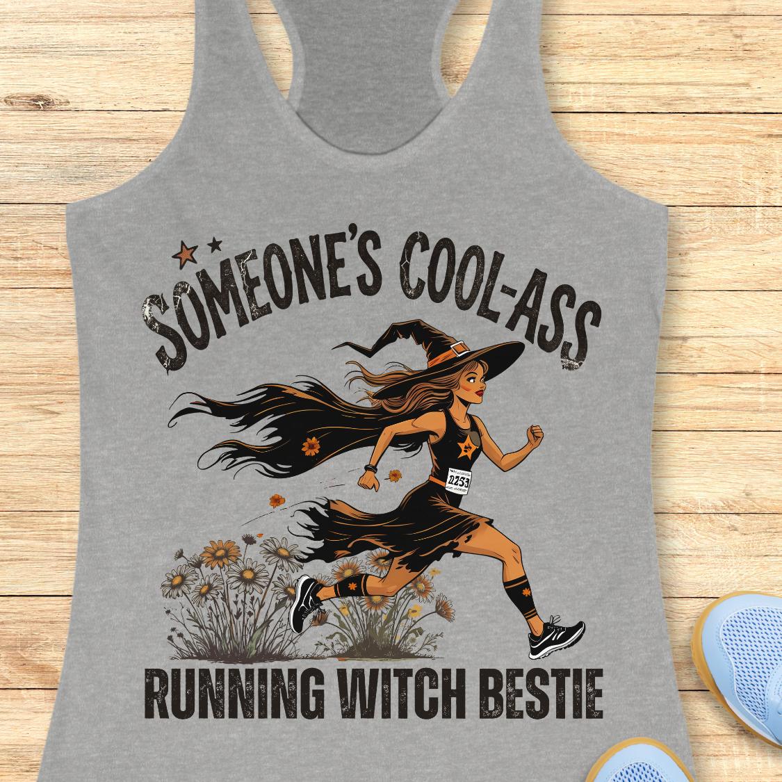 A heather gray racerback tank top laid flat on a light wood background, featuring a graphic of a running witch with the text 'SOMEONE'S COOL-ASS RUNNING WITCH BESTIE'.