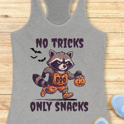 A heather gray racerback tank top laid flat on a light wood background, featuring a cartoon raccoon dressed in an orange 'BOO' costume holding a jack-o'-lantern, with the text 'NO TRICKS ONLY SNACKS' in dark purple.