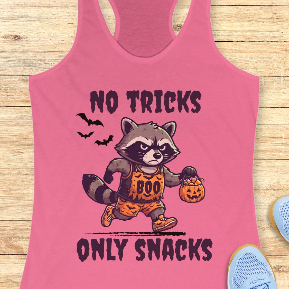 A pink racerback tank top laid flat on a light wood surface, featuring a cartoon raccoon dressed in an orange 'BOO' Halloween outfit holding a jack-o'-lantern, with the text 'NO TRICKS ONLY SNACKS' in dark lettering.