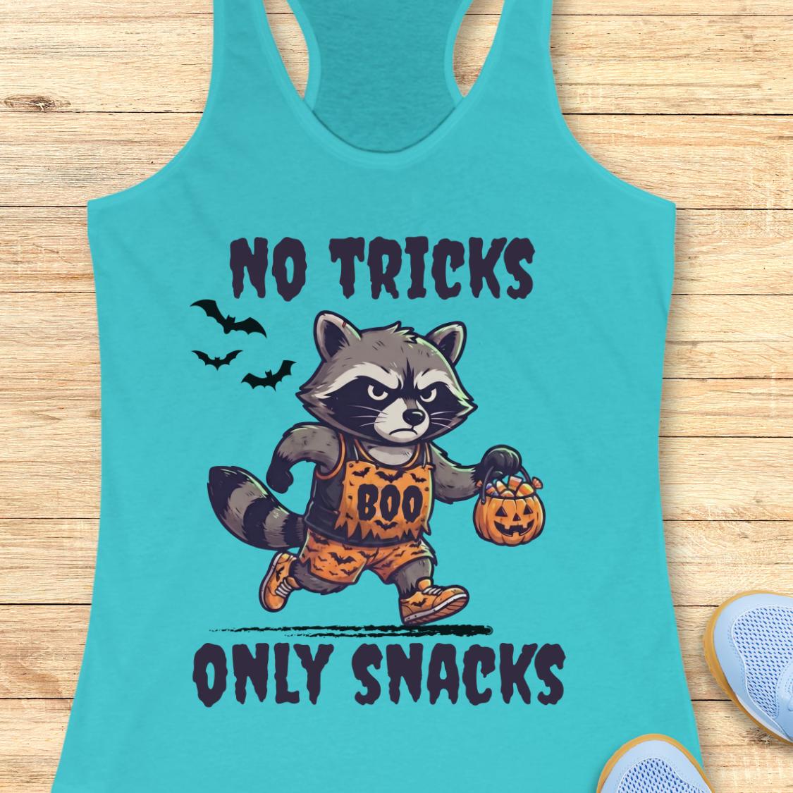 A turquoise racerback tank top laid flat on a light wood surface, featuring a cartoon raccoon in a Halloween costume holding a pumpkin bucket and the text 'NO TRICKS ONLY SNACKS.' A partial blue shoe is visible at the lower right edge.