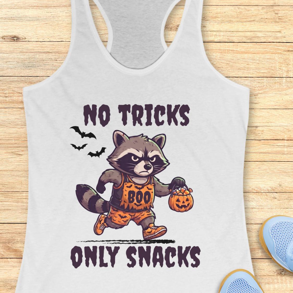 A white racerback tank top laid flat on a light wood background, featuring a cartoon raccoon dressed as Boo holding a pumpkin bucket with the text 'NO TRICKS ONLY SNACKS'.