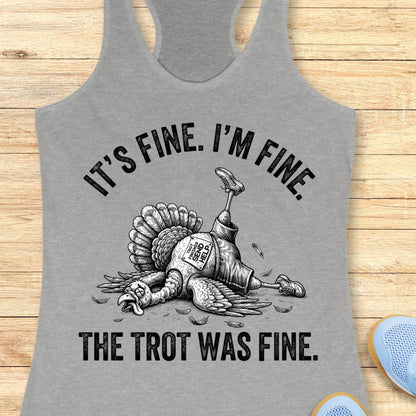 A heather gray racerback tank top laid flat on a light wood background, featuring a black graphic of a lying turkey with a prosthetic leg and the text 'IT'S FINE. I'M FINE.