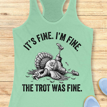 A mint green racerback tank top laid flat on a light wood background, featuring a black graphic of a dead turkey with a running leg and the text 'IT'S FINE. I'M FINE.