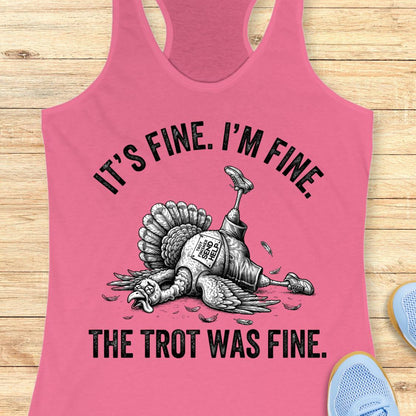 A pink racerback tank top laid flat on a light wood surface, featuring a black graphic of a lying turkey with the text 'IT'S FINE. I'M FINE.