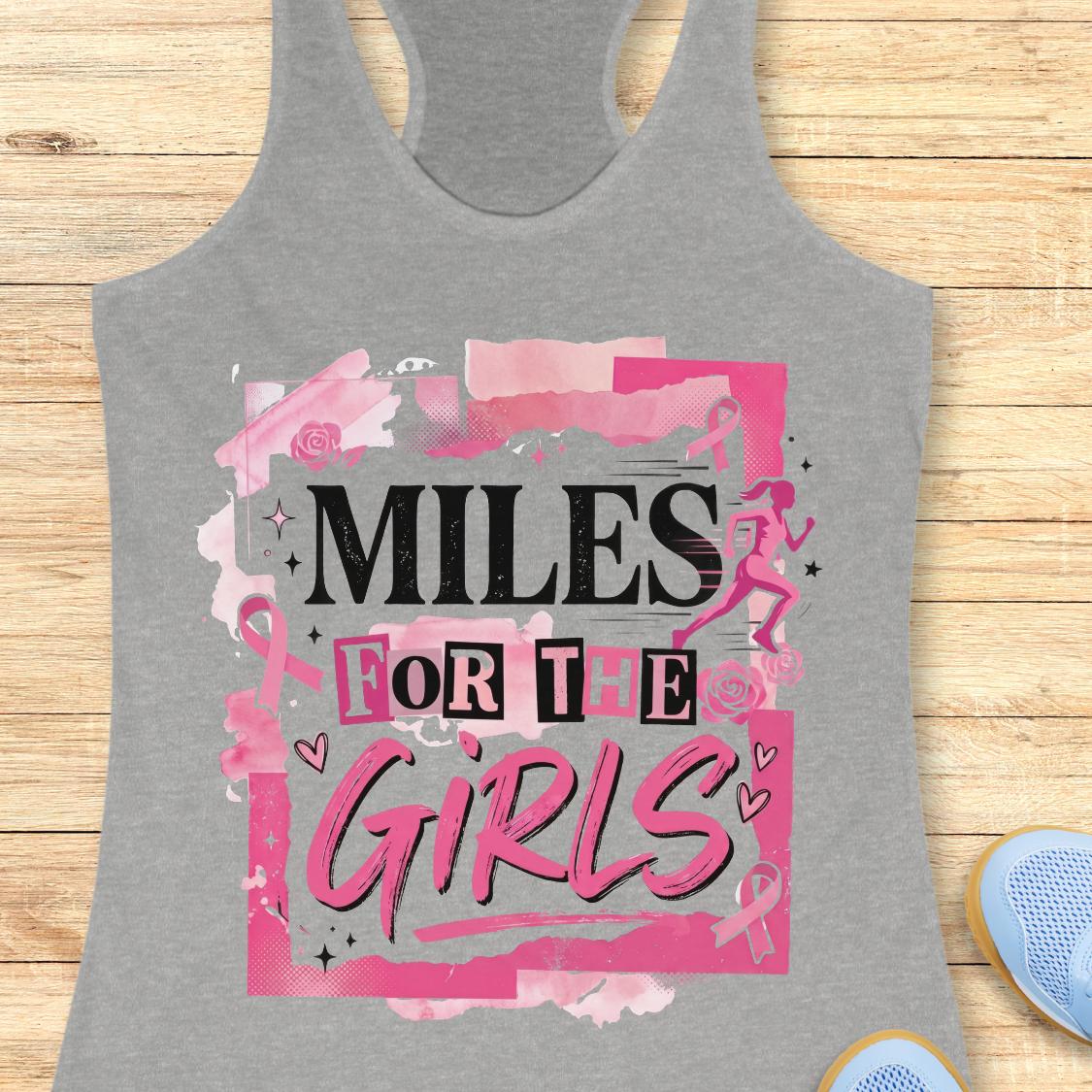 A heather gray racerback tank top with a pink and black graphic that reads 'MILES FOR THE GIRLS' on a light wood background, with partial blue sneakers visible at the bottom corners.