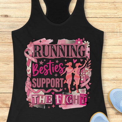 A black racerback tank top with a pink and black graphic that reads 'running besties support the fight' in stylized lettering, surrounded by pink ribbon motifs and small runner silhouettes, shown on a wooden plank background with partial blue shoes at the edges.