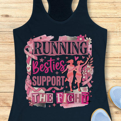 A navy racerback tank top with a pink and black graphic that reads 'running besties support the fight' in stylized lettering, surrounded by pink ribbon motifs and small runner silhouettes, shown on a wooden plank background with partial blue shoes at the edges.