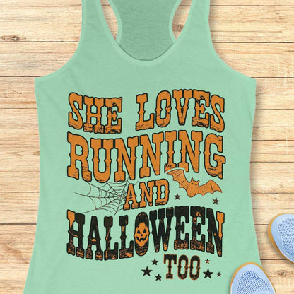 A mint racerback tank top laid flat on a light wood plank background, featuring a large Halloween-themed graphic that reads 'SHE LOVES RUNNING AND HALLOWEEN TOO' in orange and black distressed lettering, with spiderwebs, bats, and stars.